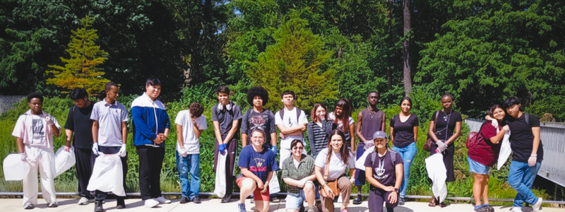 group shot of Liberty Promise High School students with EcoAction Arlington staff holding trash bags with green trees and fauna in the background