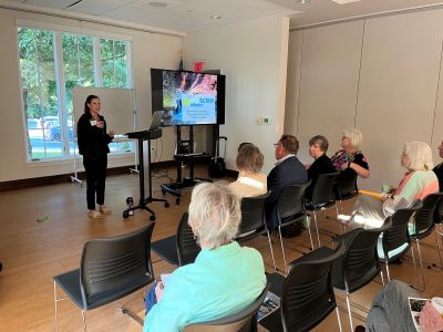 Kara Simon presenting in front of attendies sitting in rows of chairs